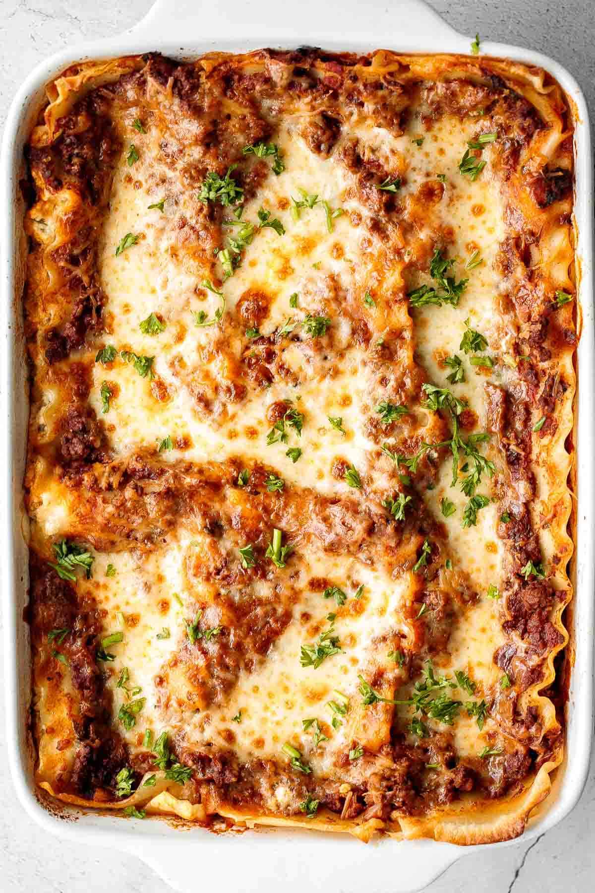 Baked lasagna in a white rectangular dish, topped with melted cheese, tomato sauce, and chopped parsley—perfect for Sunday Dinner Ideas or classic Family Dinner Recipes.
