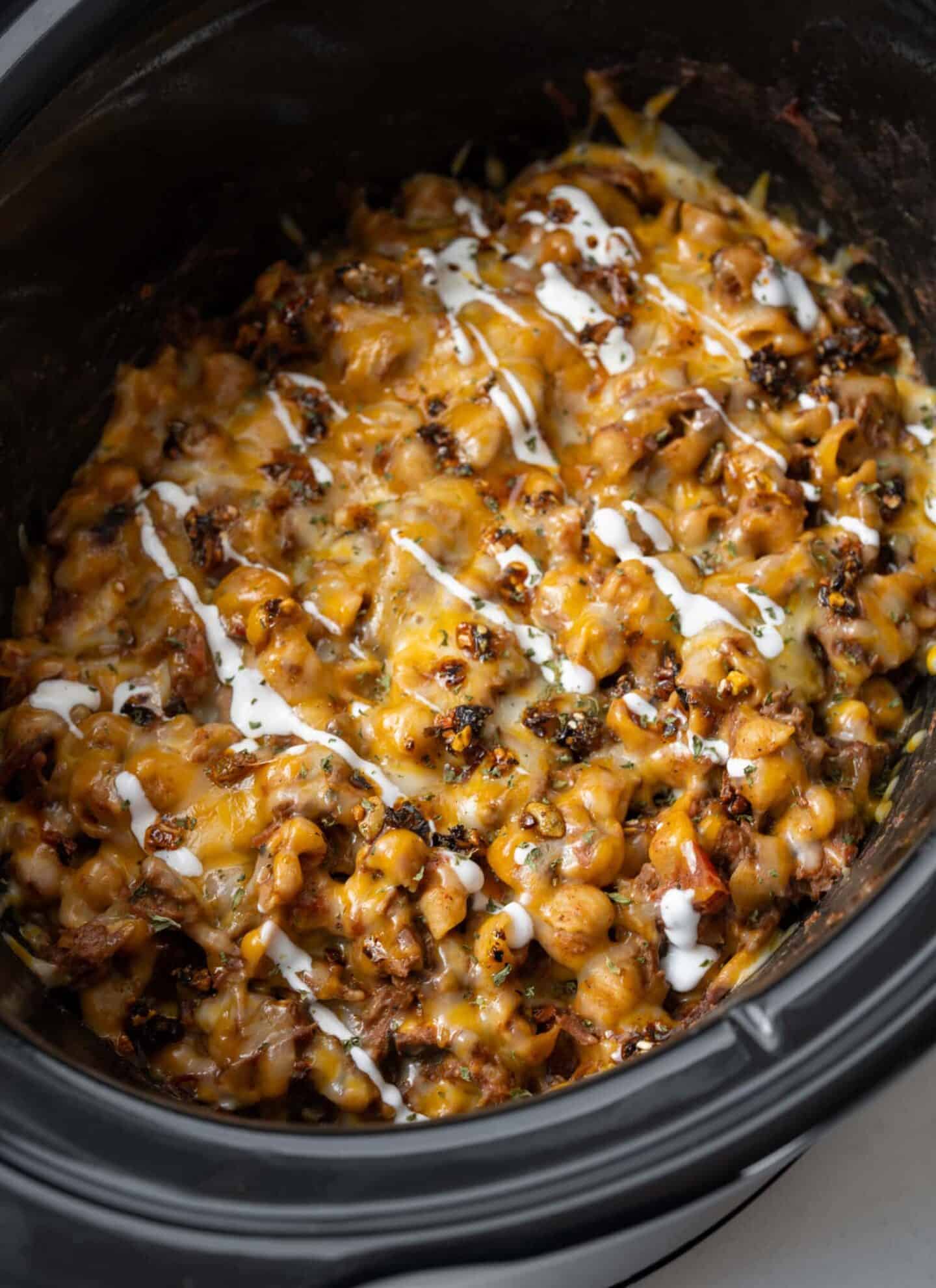 A cheesy, high protein mixture of beans, corn, and sauce is cooked in a slow cooker with a drizzle of sour cream on top—perfect for fans of easy crockpot recipes.