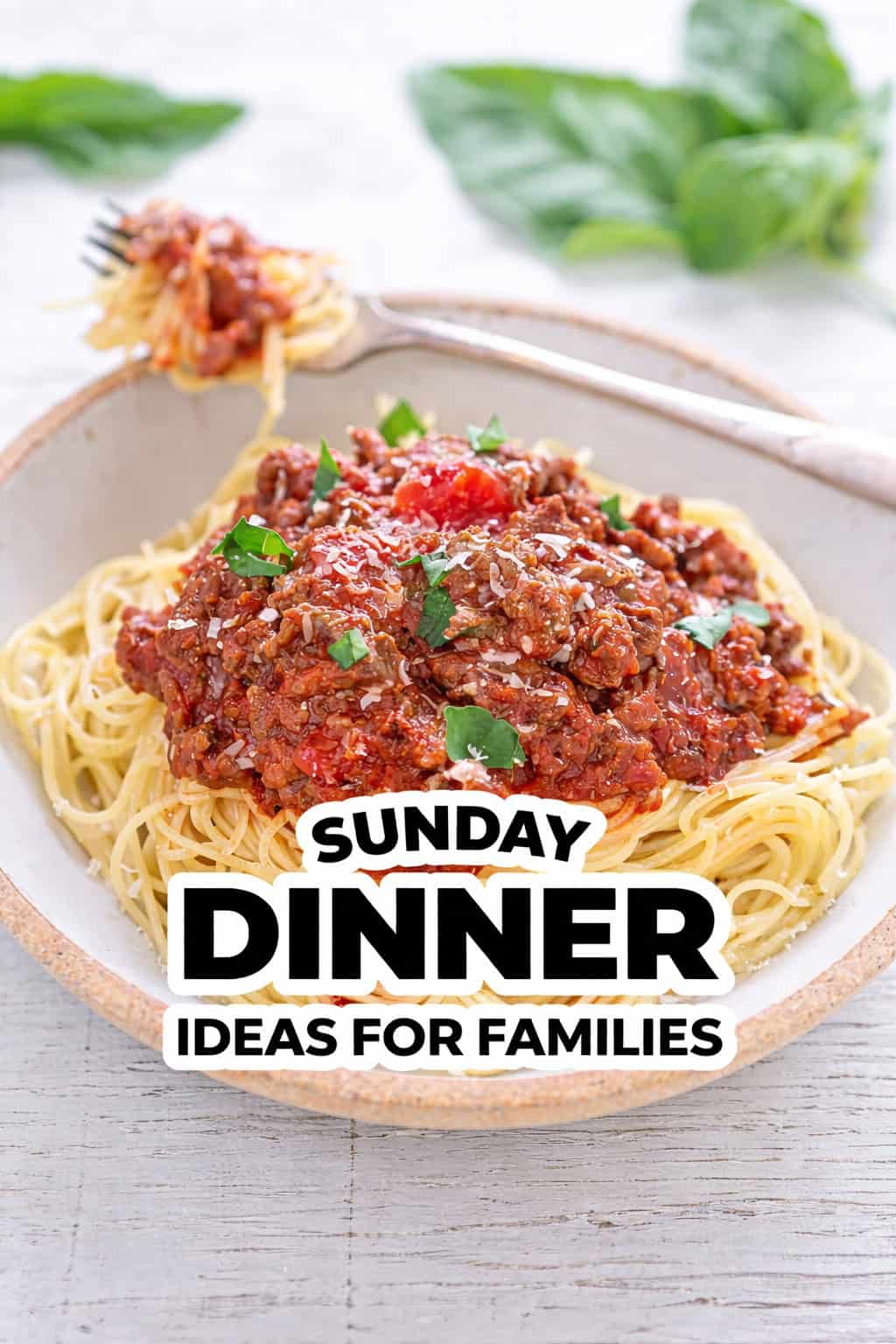 A plate of spaghetti topped with meat sauce and parsley, with a forkful of pasta in the background. Text overlay reads, "Sunday Dinner Ideas for Families"—perfect for your next Family Dinner.
