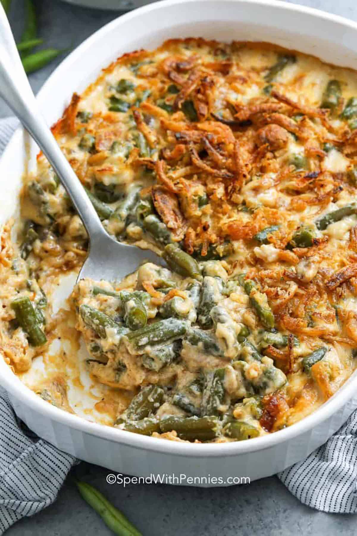 Baked green bean casserole with creamy sauce and crispy onions, served in a white dish with a spoon scooping a portion—a classic choice for Easter party food.