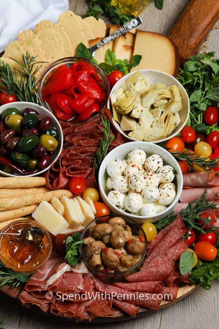 Charcuterie board with assorted meats, cheeses, marinated vegetables, olives, breadsticks, cherry tomatoes, and fresh herbs arranged on a wooden platter—perfect for Italian Potluck Ideas or as one of your favorite Potluck Dishes.