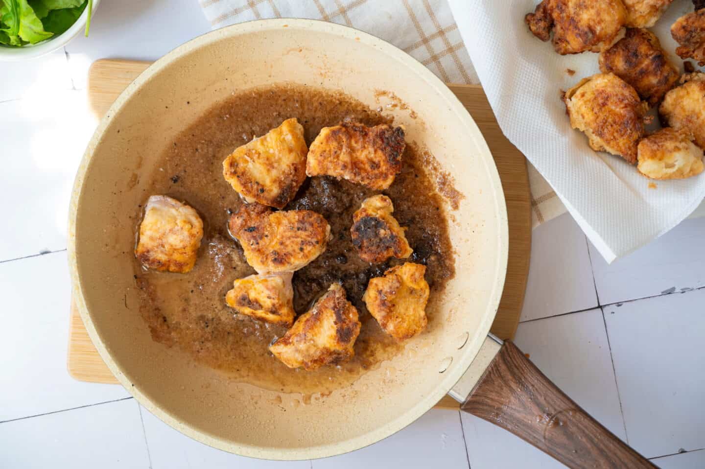 Pieces of browned Bang Bang Chicken frying in a skillet with oil, with cooked pieces resting on a paper towel on the side—perfect for assembling your own Bang Bang Chicken Rice Bowl.