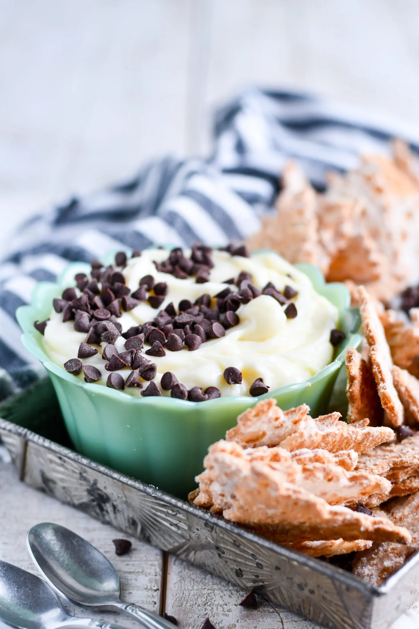 A green bowl filled with creamy dip topped with chocolate chips, surrounded by crispy crackers on a tray—perfect for Italian potluck gatherings and creative potluck ideas.
