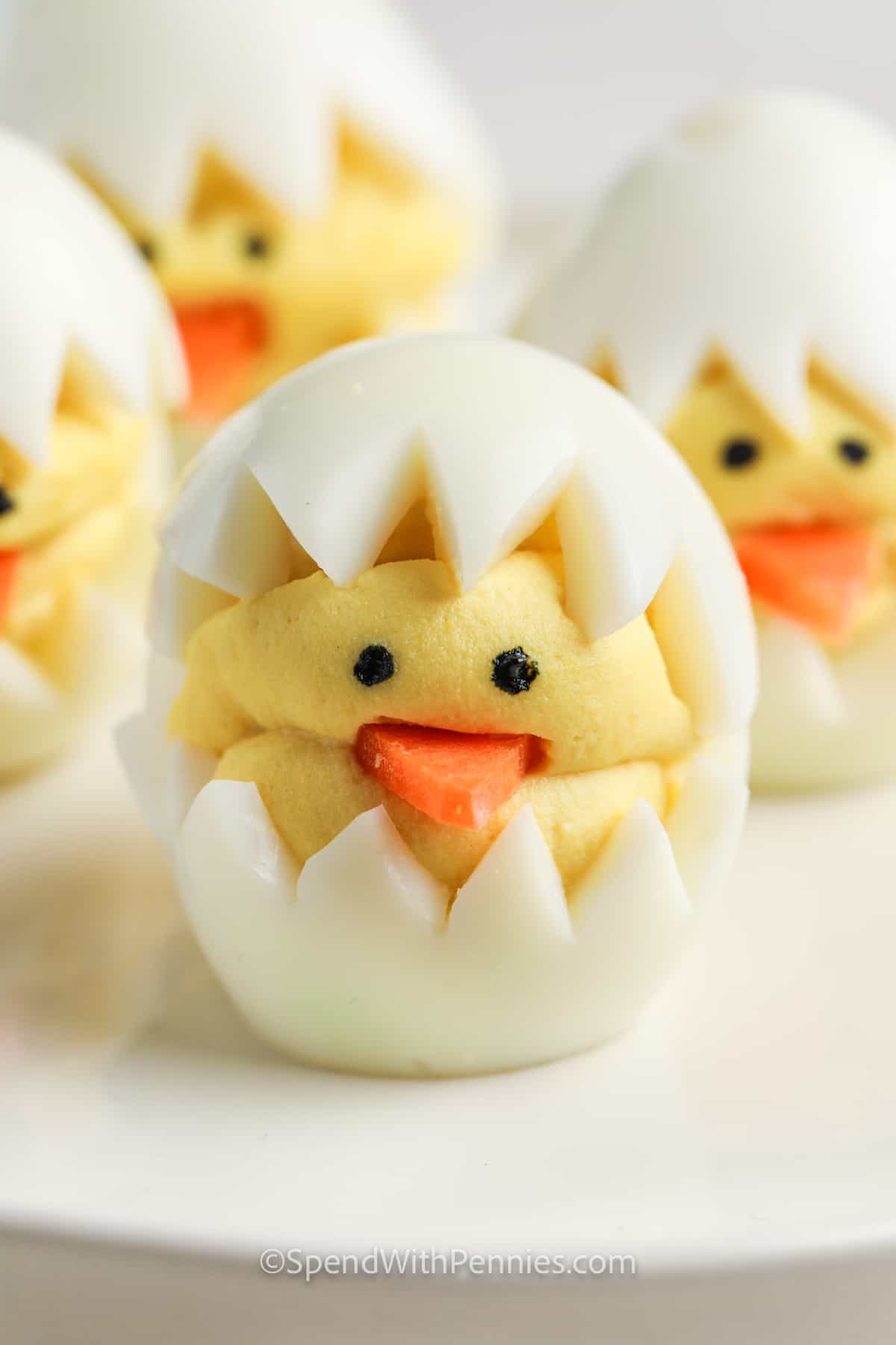 Hard-boiled eggs with zig-zag cut tops, filled and decorated to resemble baby chicks using yolk mixture, carrots, and olives—these adorable treats are perfect as Easter side dishes or for your collection of festive Easter recipes.