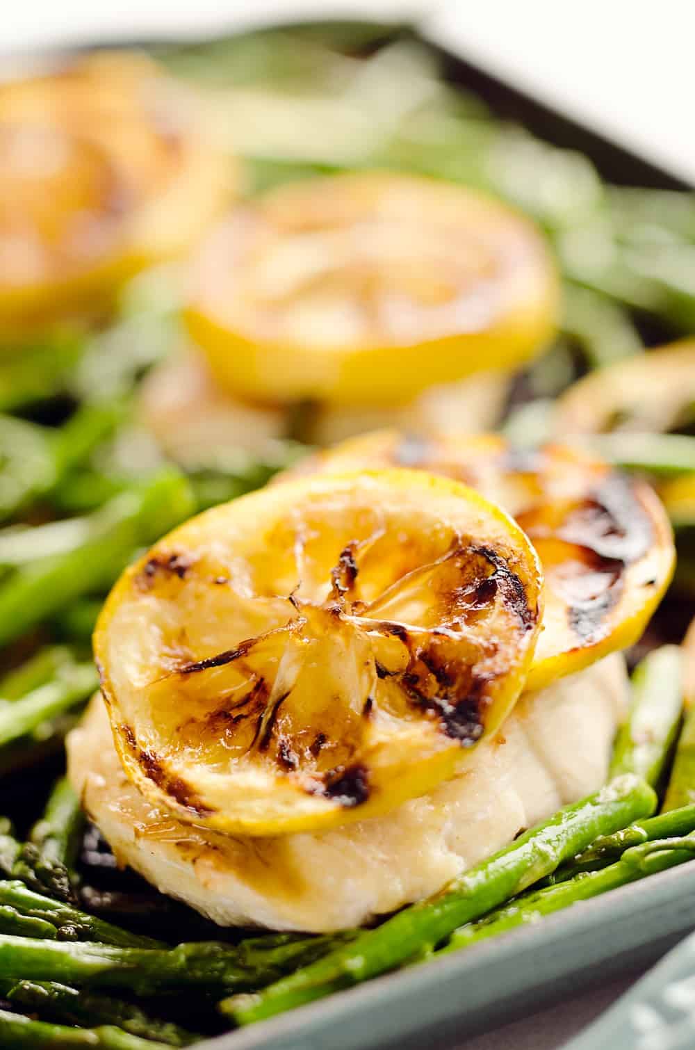 Grilled lemon slices top a piece of cooked fish, served with asparagus spears on a baking tray—perfect for fresh spring dinner party menu ideas.