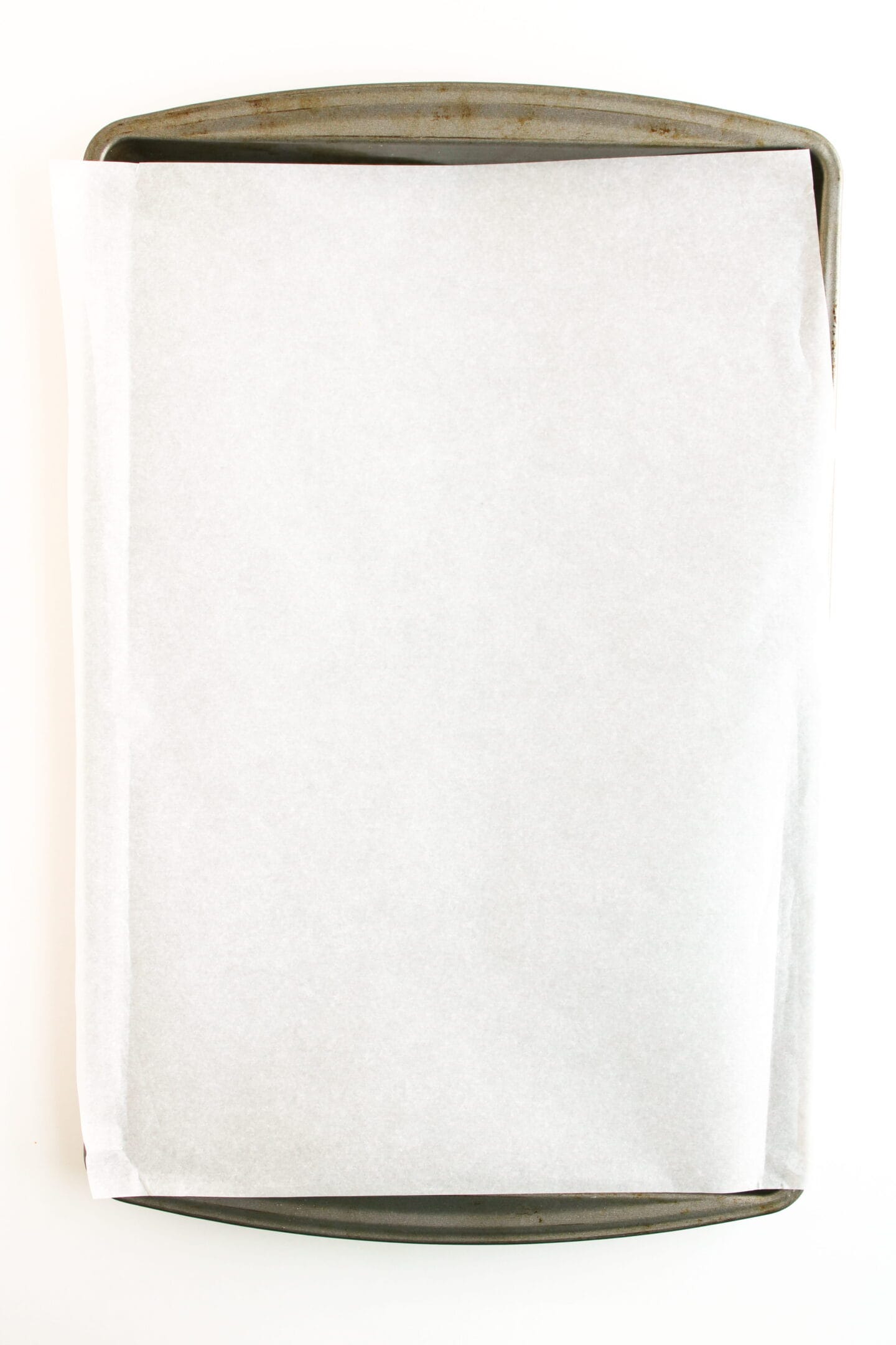 A metal baking sheet covered with a large piece of parchment paper, perfect for baking Ham and Cheese Crescent Rolls, viewed from above on a white background.