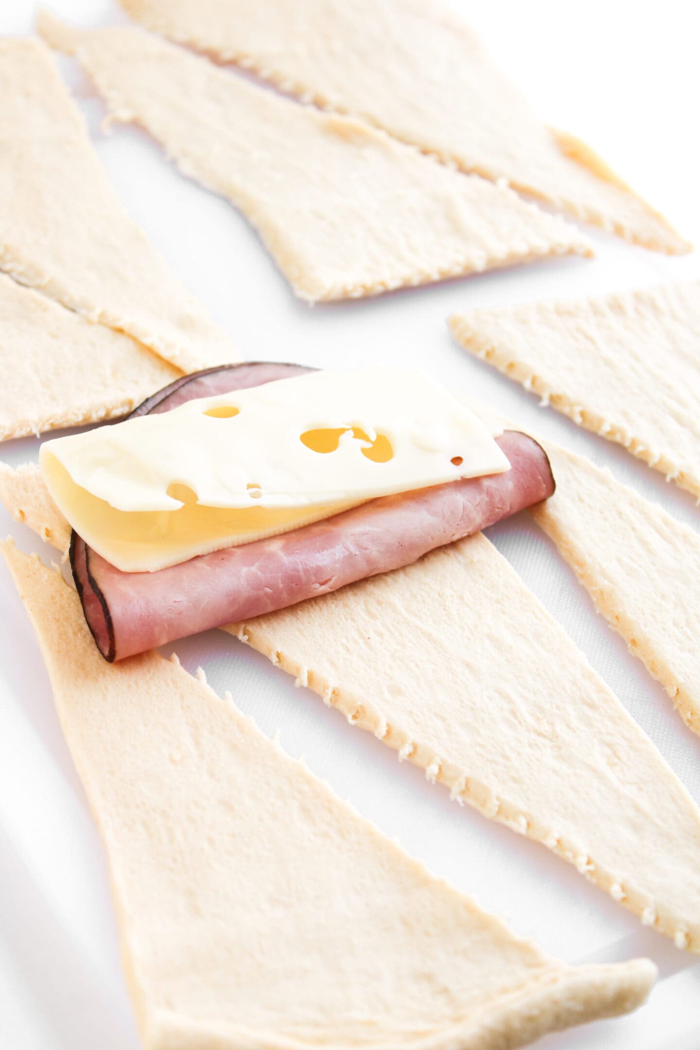 Unbaked crescent roll dough triangles with ham and Swiss cheese on one, ready to be rolled up for delicious ham and cheese crescent rolls—a classic favorite among easy crescent roll recipes.