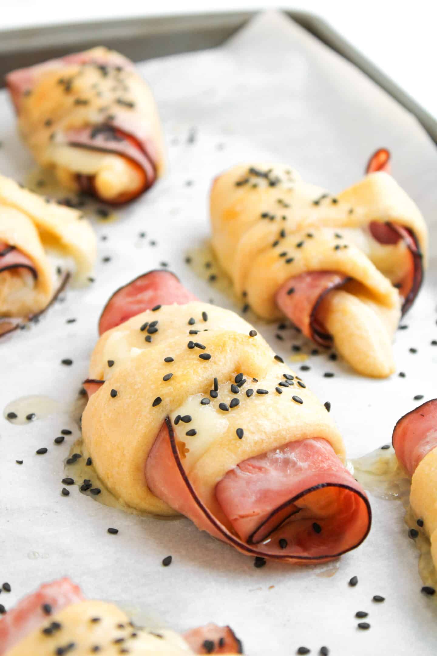 Golden Ham and Cheese Crescent Rolls filled with savory ham, topped with black sesame seeds, baked to perfection on a parchment-lined sheet.