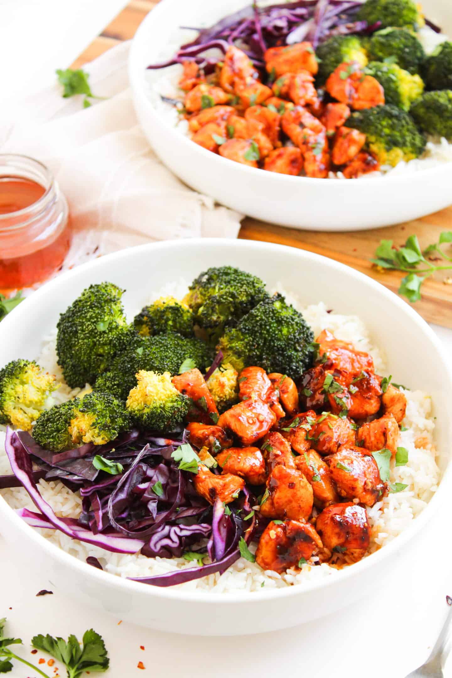 A Chicken Bowl featuring white rice, cooked broccoli, shredded red cabbage, and saucy chicken pieces, garnished with chopped herbs. Try this Hot Honey Chicken Bowl for a flavorful twist on a classic favorite!.