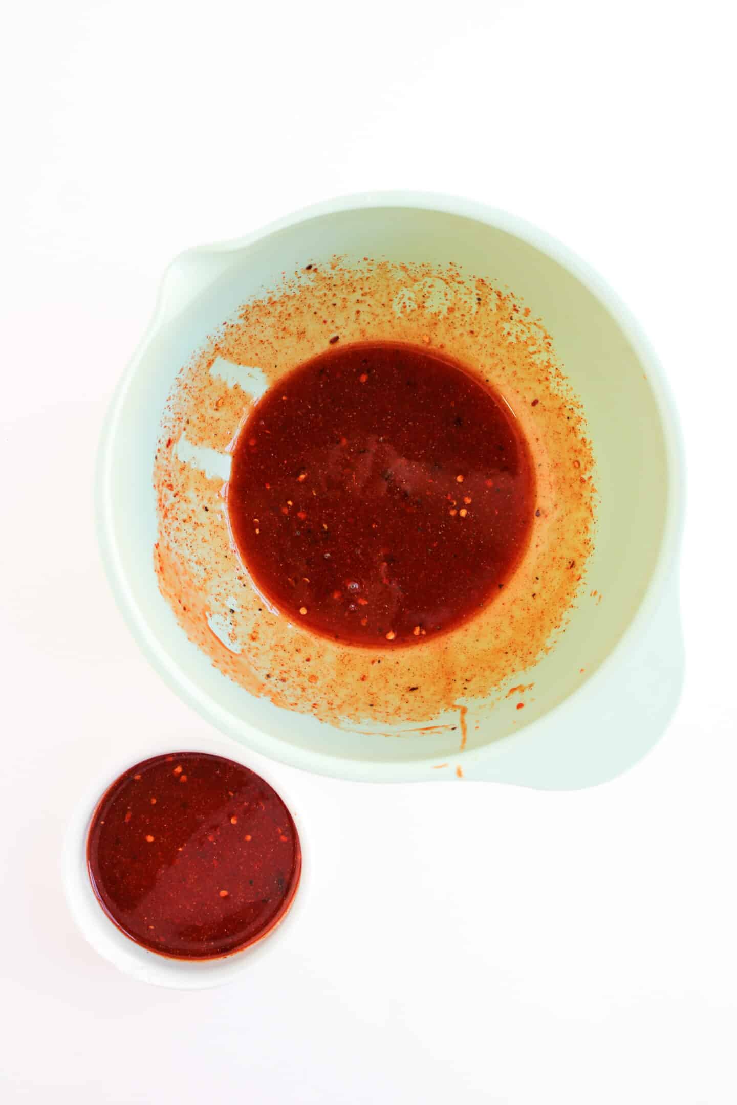 A large mixing bowl and a small bowl, both filled with Hot Honey Chicken marinade, are placed on a white surface.