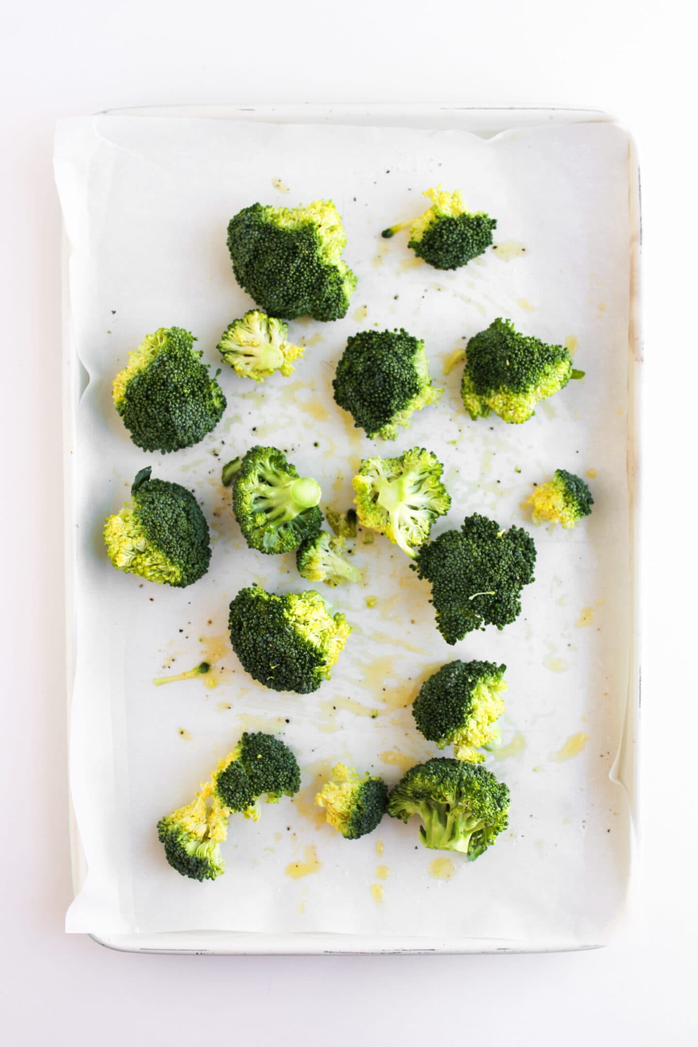 Broccoli florets spread on a parchment-lined baking sheet, lightly drizzled with oil, make the perfect side for a Hot Honey Chicken Bowl, ready for roasting.