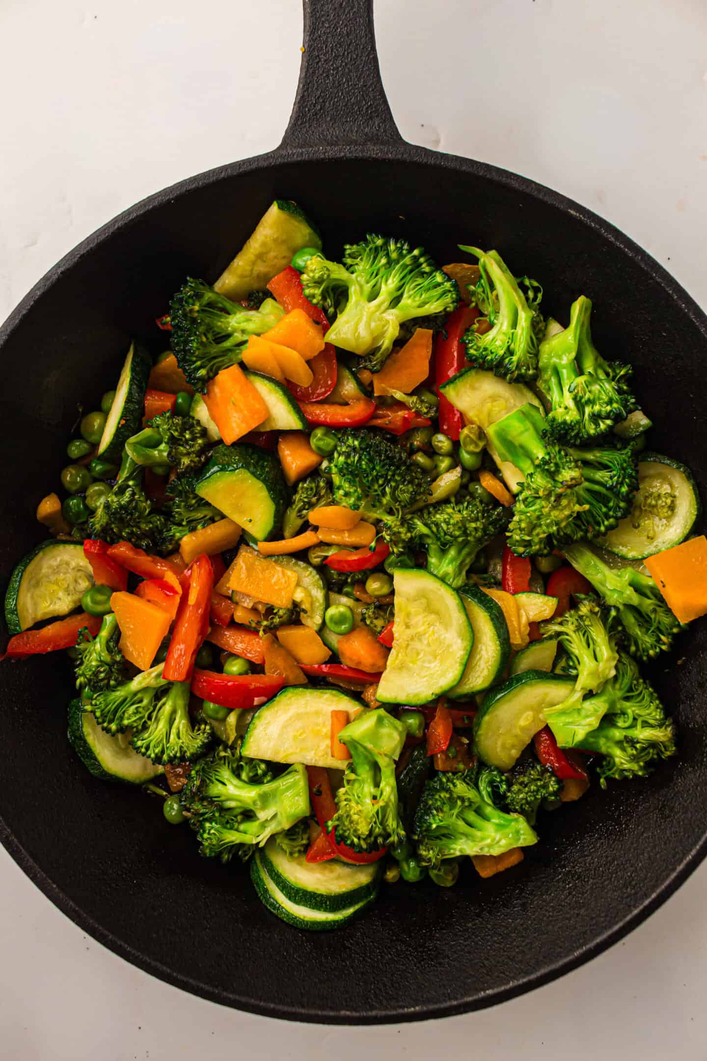 A black skillet filled with sautéed mixed vegetables—like broccoli, zucchini, red bell pepper, carrots, and peas—on a white surface, perfect for a fresh Pasta Primavera or as a colorful Italian dish.