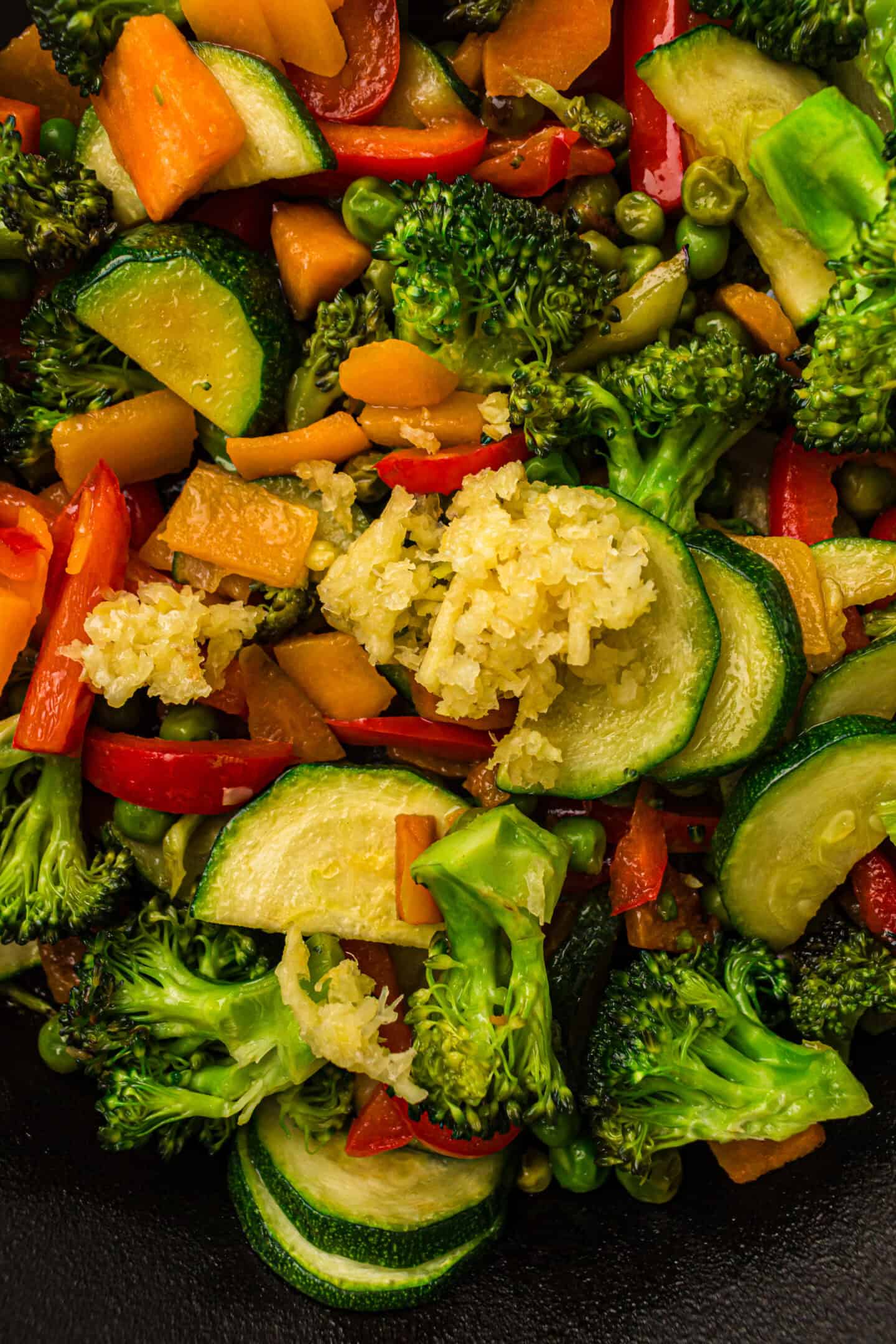 A close-up of a vibrant vegetable stir-fry for Pasta Primavera, featuring broccoli, zucchini, red bell pepper, carrots, and a small pile of minced garlic—perfect for your next vegetarian pasta recipe.