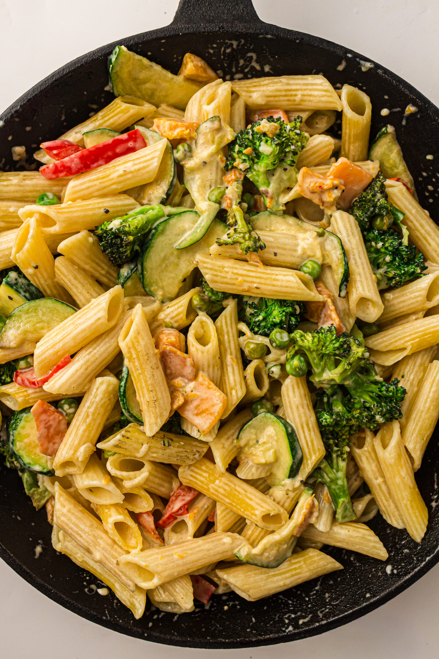 Penne Pasta Primavera with broccoli, zucchini, and red bell pepper in a creamy sauce, served in a black skillet.
