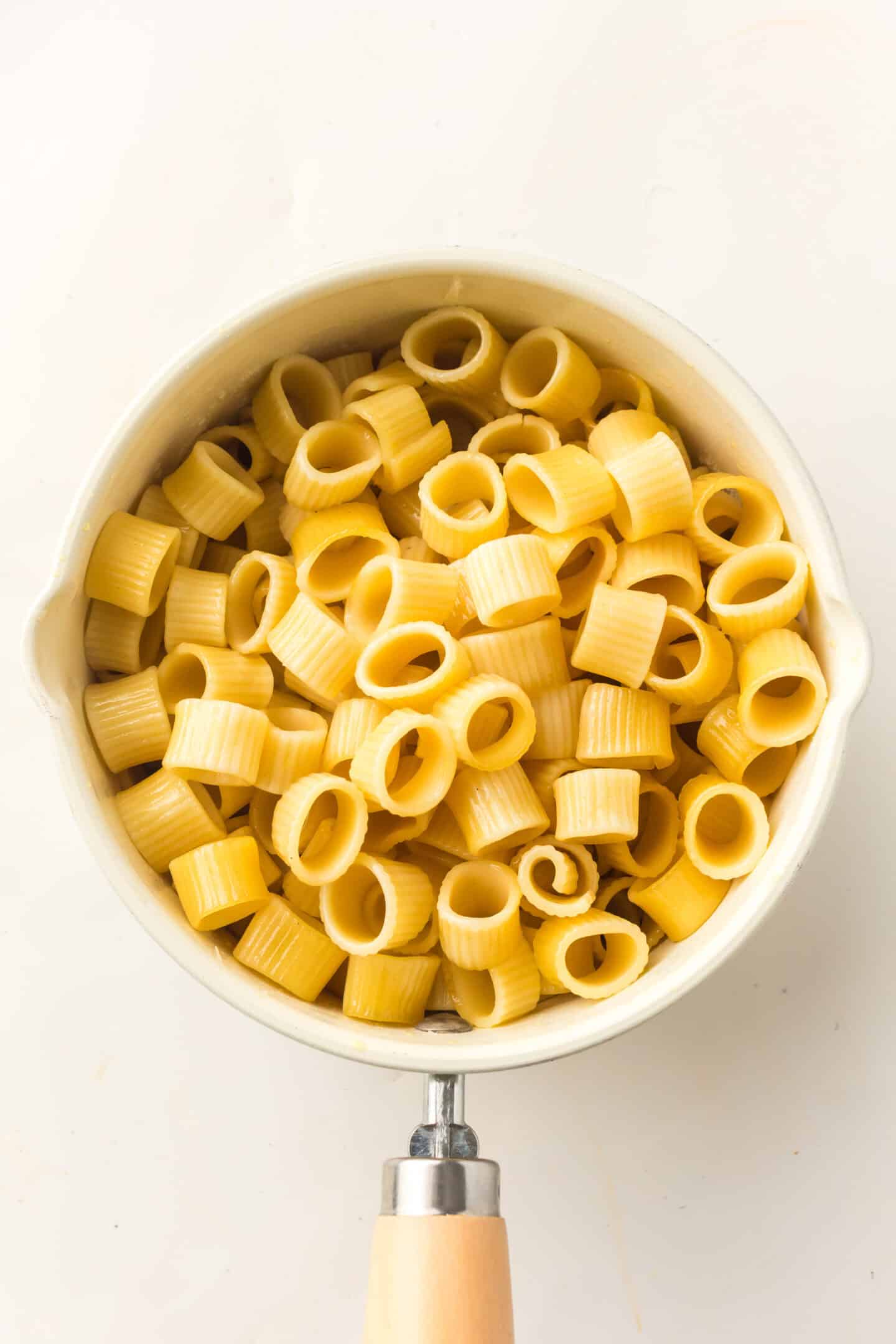A saucepan filled with cooked ditalini pasta and peas, viewed from above on a white background.