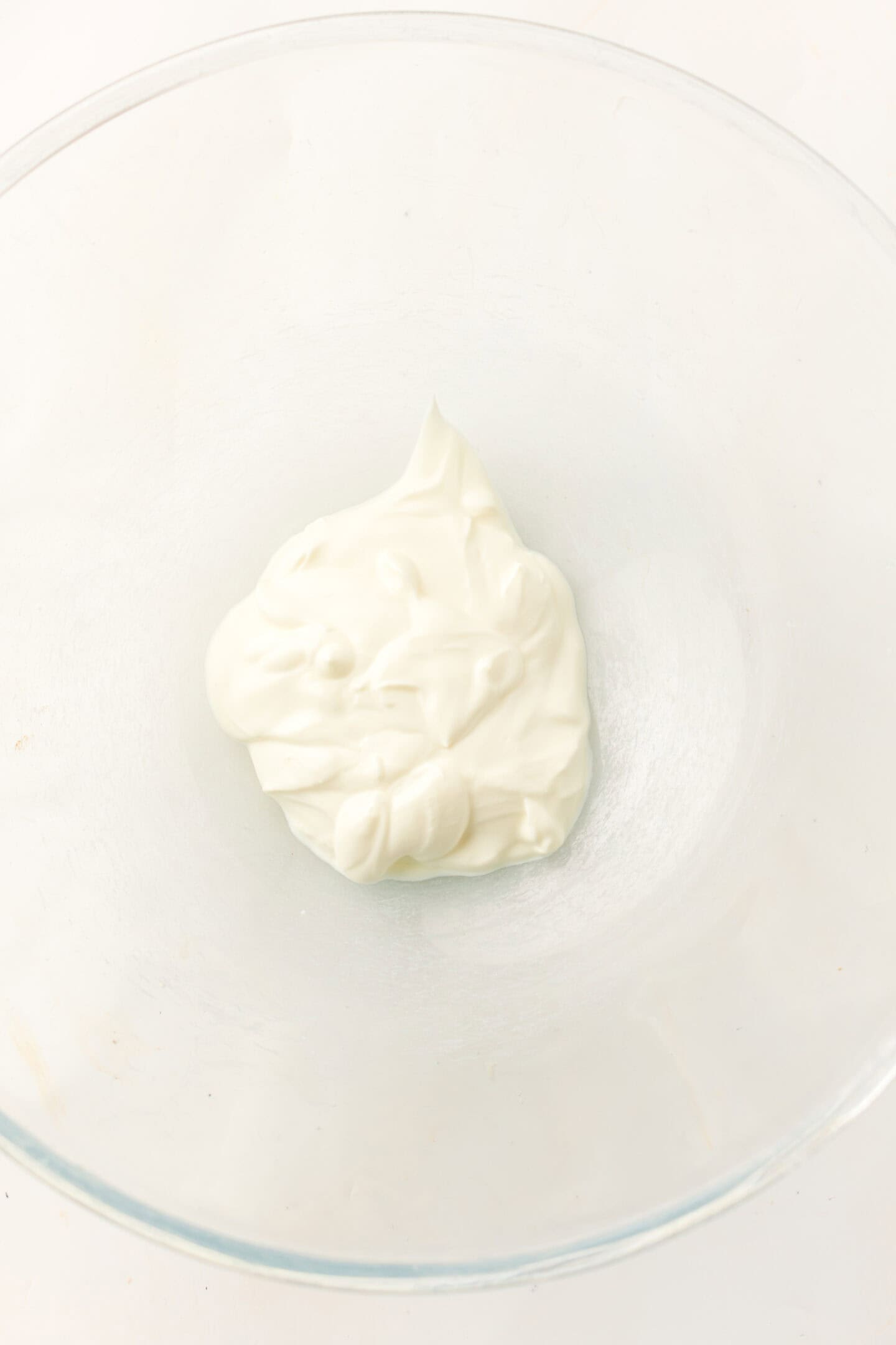 A dollop of white yogurt or sour cream in a clear glass bowl on a white surface, perfect for topping chicken pasta salad.
