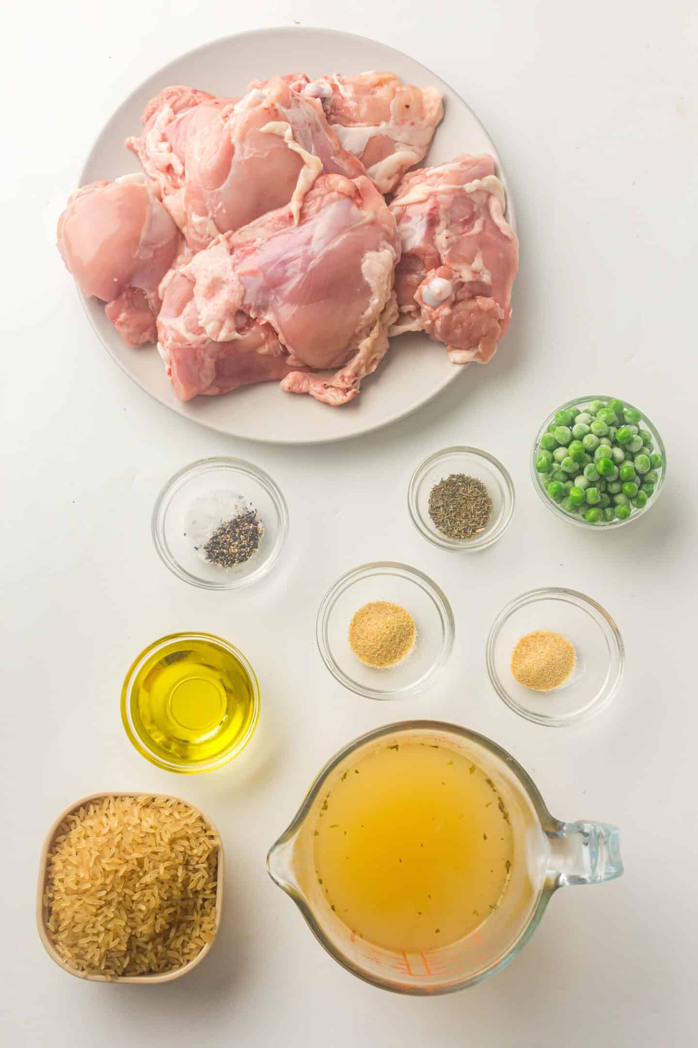 Plate of raw chicken thighs, bowls of frozen peas, dry rice, olive oil, chicken broth, black pepper, garlic powder, onion powder, and salt arranged on a white surface—perfect for an easy Instant Pot meal.