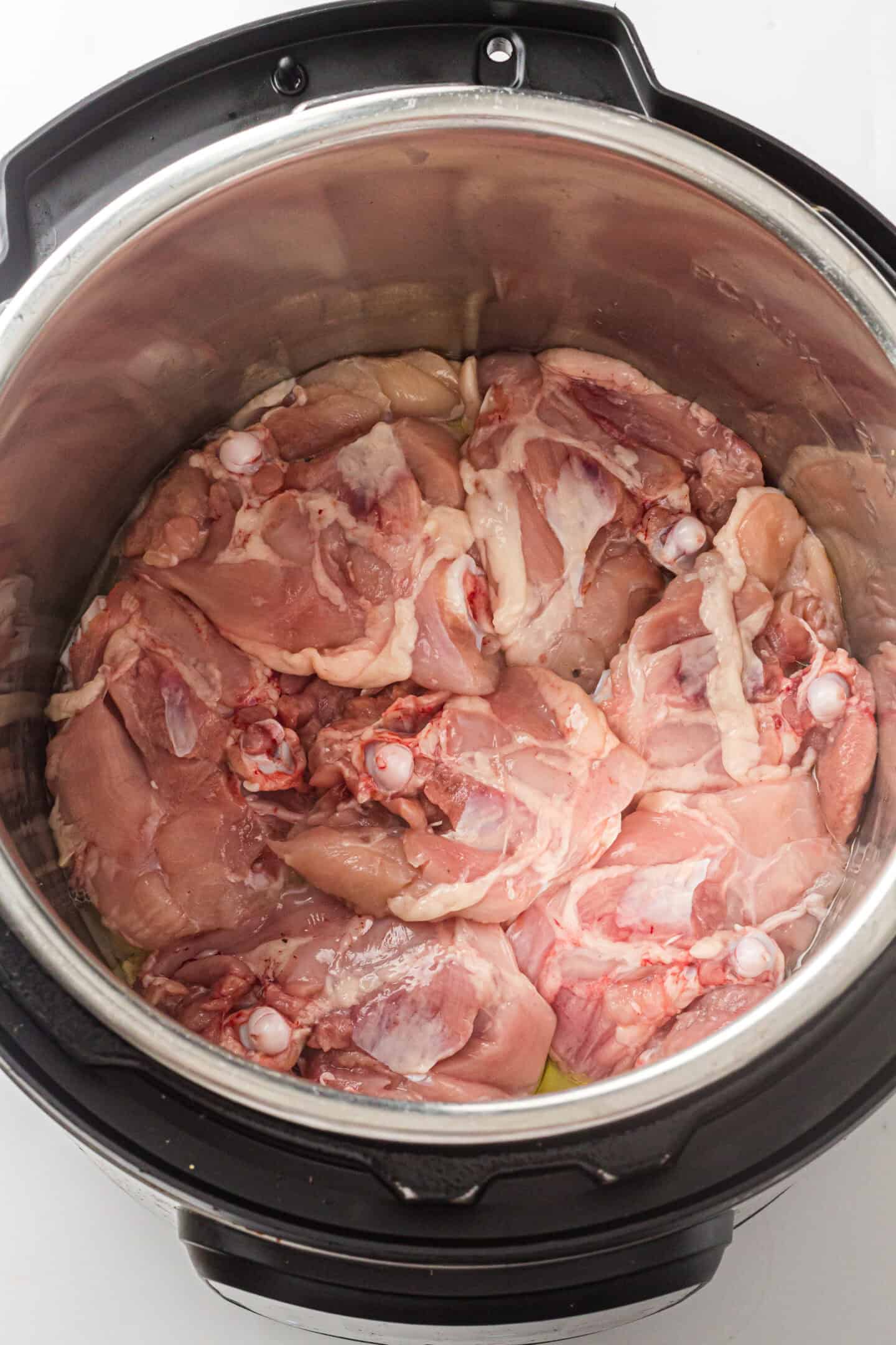 Raw chicken thighs arranged in a single layer inside an Instant Pot before cooking, ready to be paired with rice for a delicious meal.