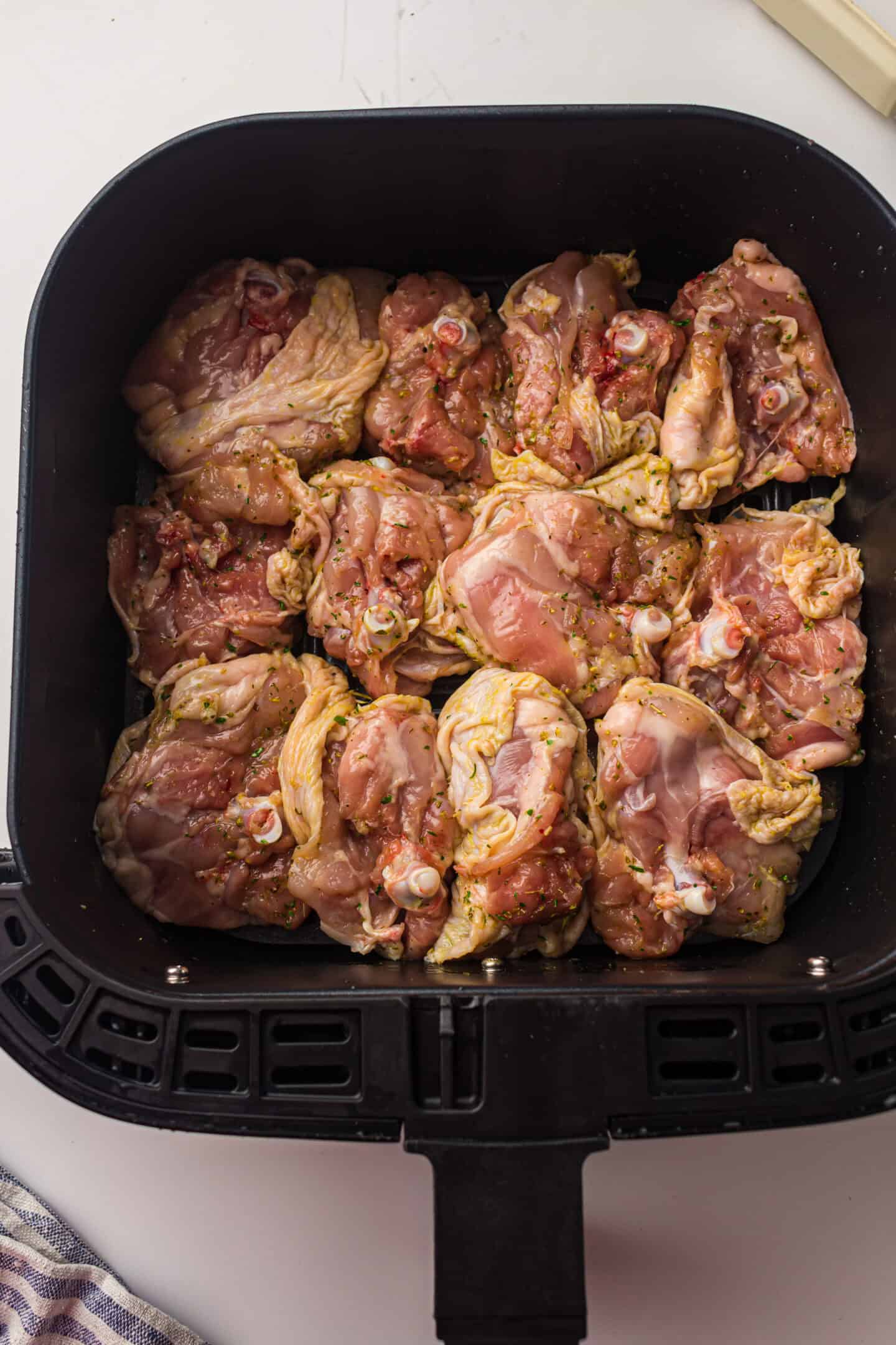 Raw, marinated chicken thighs are arranged in a single layer inside the air fryer basket, ready to be cooked into delicious air fryer chicken thighs.