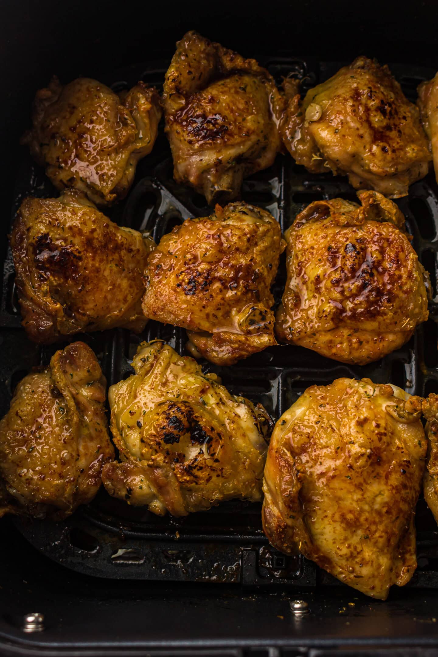 Nine cooked, seasoned chicken thighs are arranged in a single layer inside an air fryer basket, making this a perfect example of easy and delicious air fryer chicken.