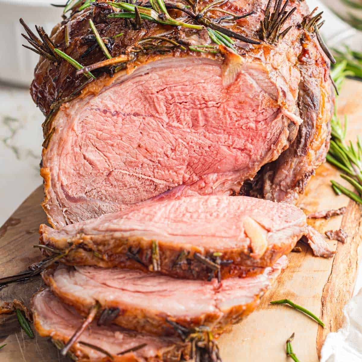 A sliced roast beef garnished with fresh rosemary sits on a wooden cutting board—an elegant choice for any Spring Dinner Party menu.