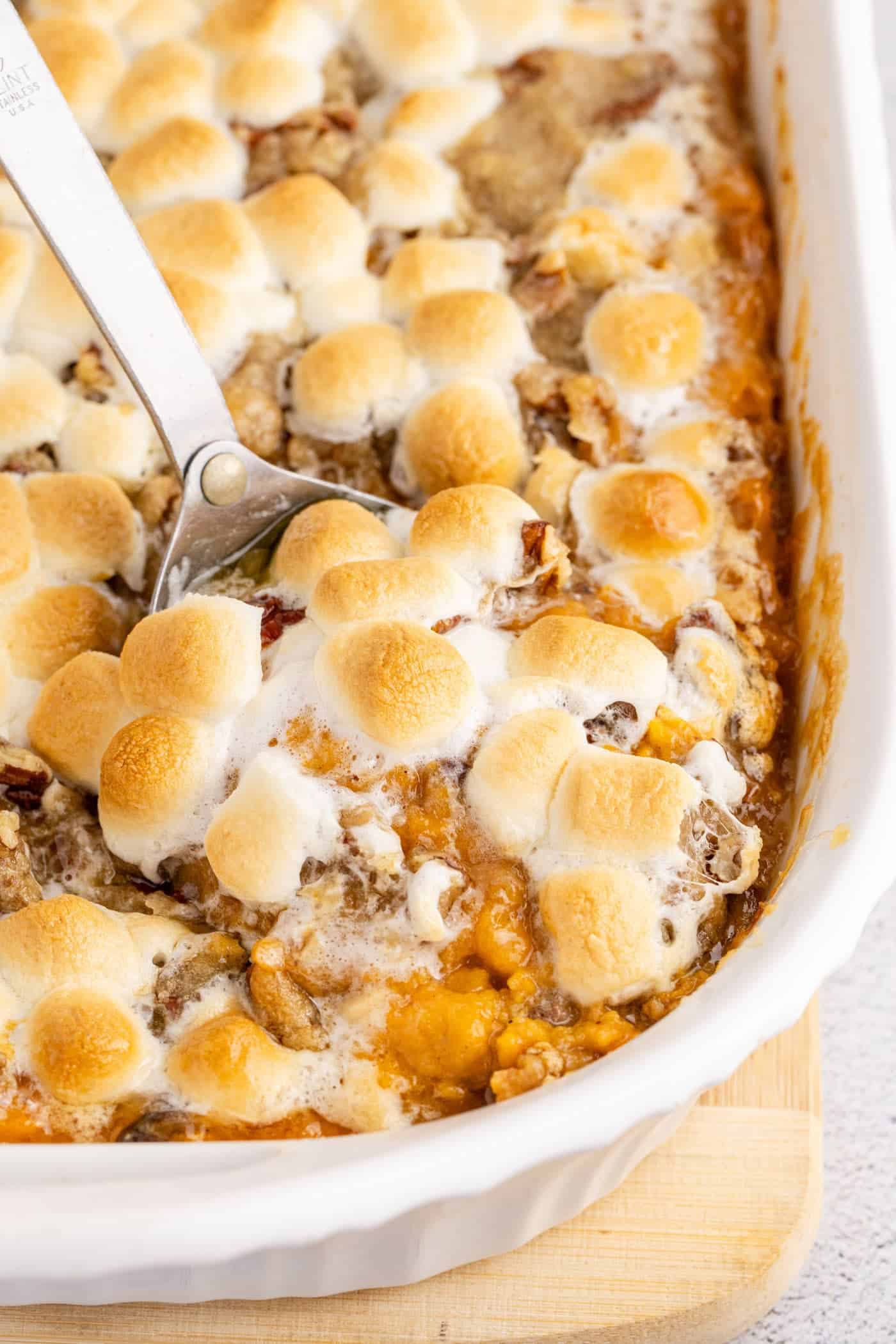 A baked casserole topped with golden-brown toasted marshmallows, with a serving spoon scooping out a portion—perfect for holiday sides or as one of your favorite Easter side dishes.