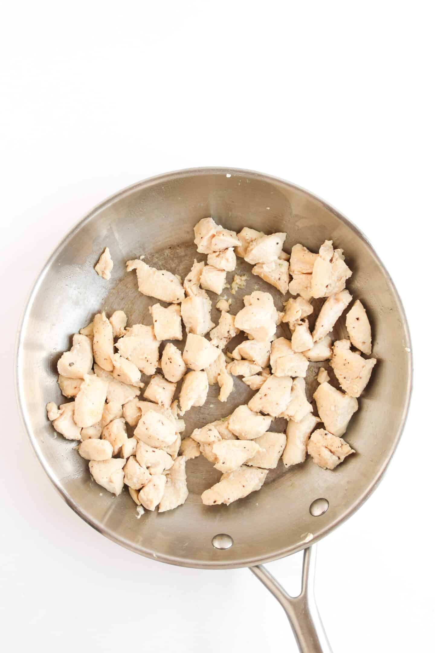 A stainless steel pan with pieces of cooked, seasoned chicken—perfect for creating delicious Teriyaki Chicken Bowls—on a white background.
