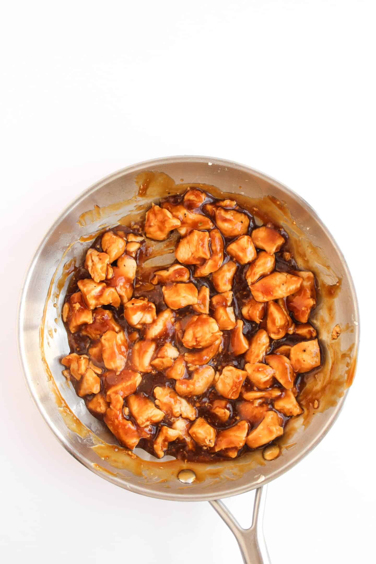 A stainless steel pan filled with Teriyaki Chicken pieces coated in a glossy brown sauce, viewed from above on a white background—perfect for serving in Chicken Bowls.