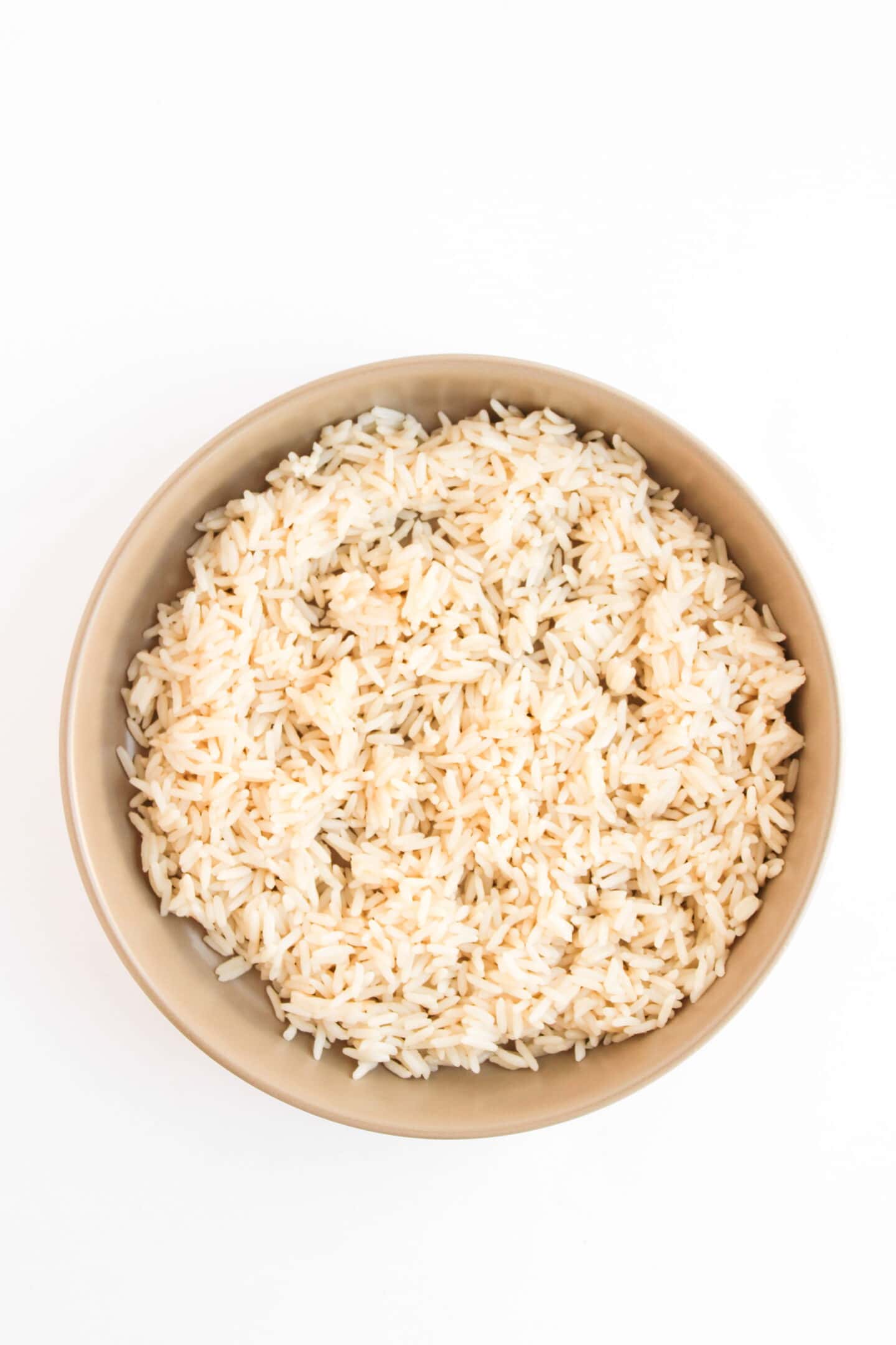 A beige bowl filled with cooked white rice, perfect for serving Teriyaki Chicken Bowls, photographed from above on a white background.