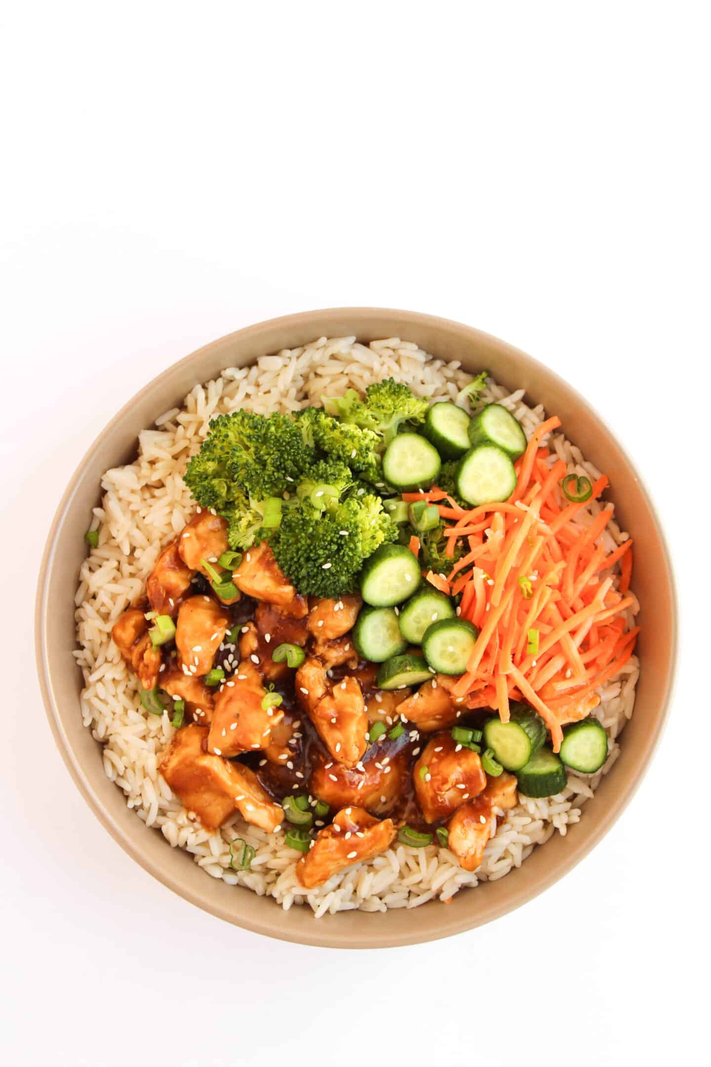 A bowl of brown rice topped with juicy Teriyaki Chicken, broccoli, sliced cucumber, shredded carrots, and green onions—perfect for fans of delicious Teriyaki Chicken Bowls.
