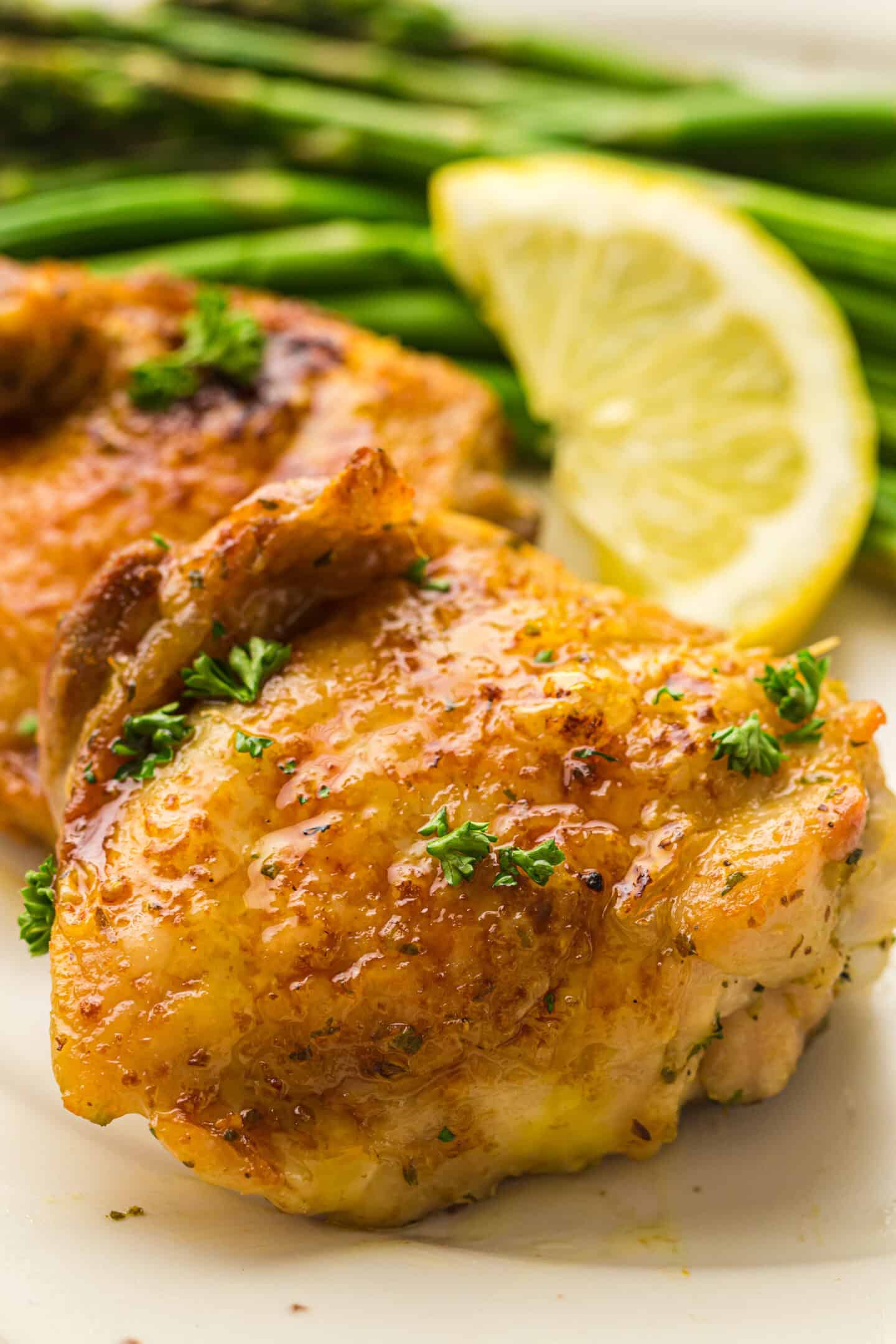 Close-up of air fryer chicken thighs garnished with parsley, served with a lemon wedge and asparagus in the background.