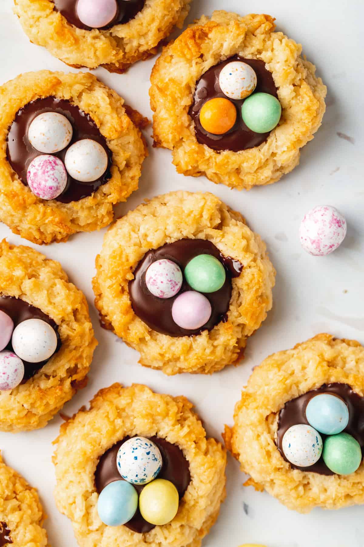 Cookies topped with a chocolate center and decorated with colorful candy eggs, these treats make the perfect Easter Party Food, beautifully arranged on a white surface.