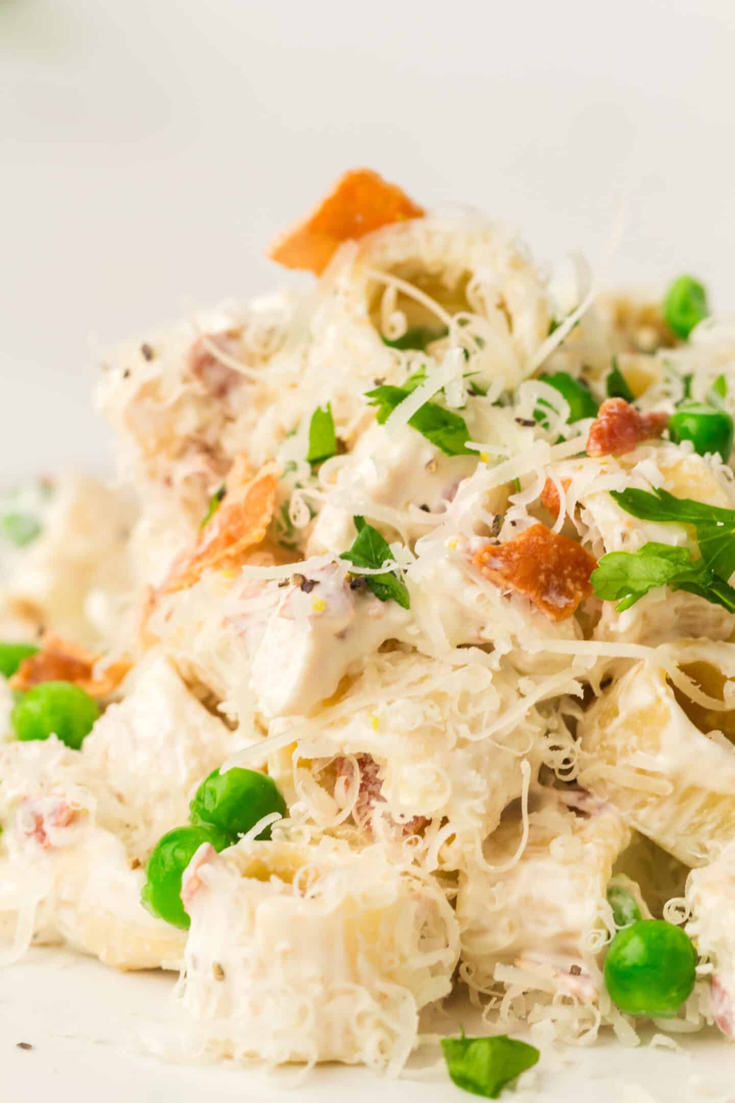 Close-up of a Light Pasta Salad featuring creamy dressing, green peas, shredded cheese, bacon bits, and chopped parsley.