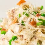 Close-up of a Light Pasta Salad featuring creamy dressing, green peas, shredded cheese, bacon bits, and chopped parsley.