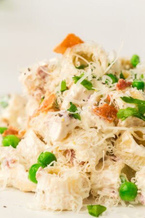Close-up of a Light Pasta Salad featuring creamy dressing, green peas, shredded cheese, bacon bits, and chopped parsley.