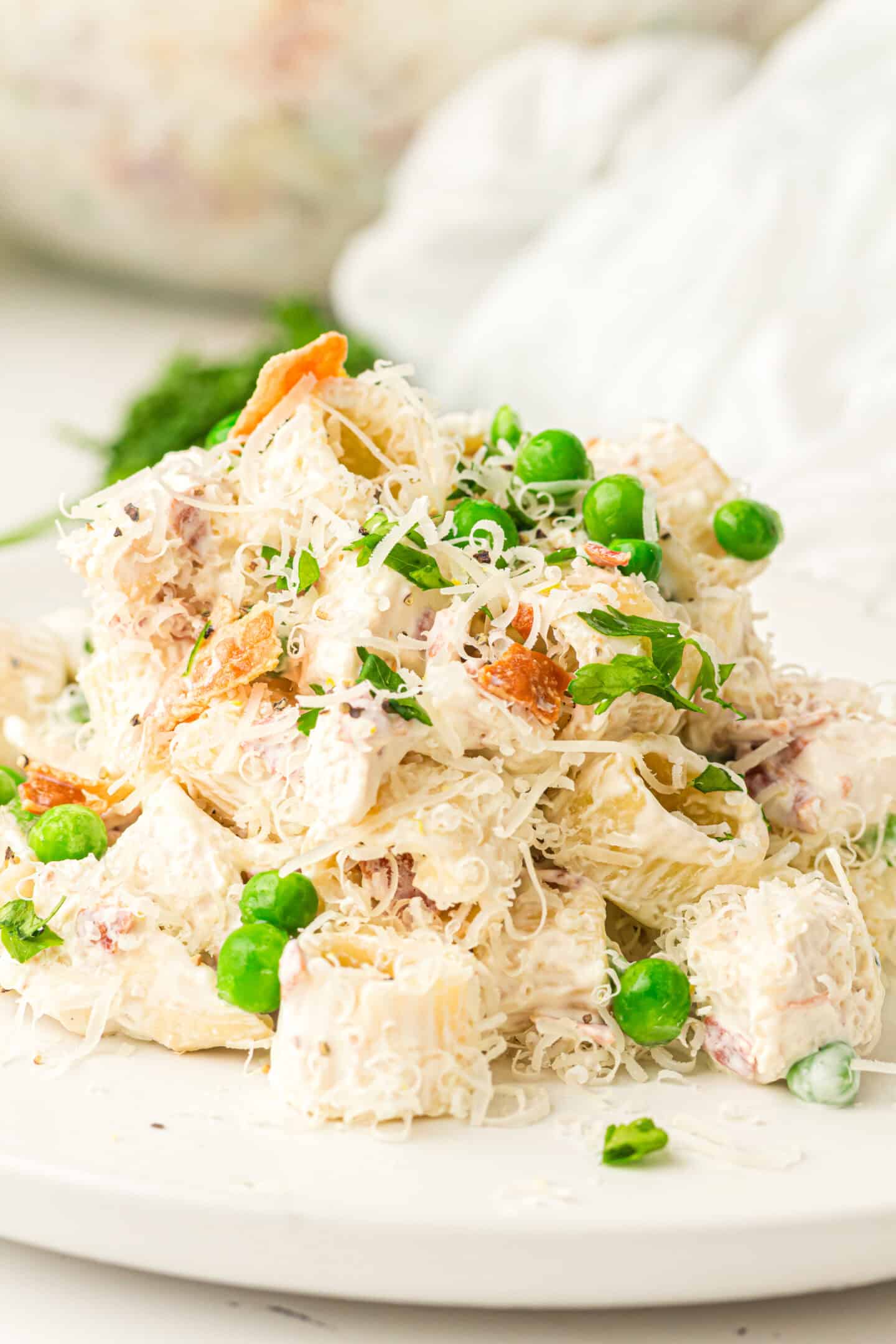 A plate of creamy Chicken Pasta Salad with green peas, shredded cheese, and pieces of bacon, served on a white plate.