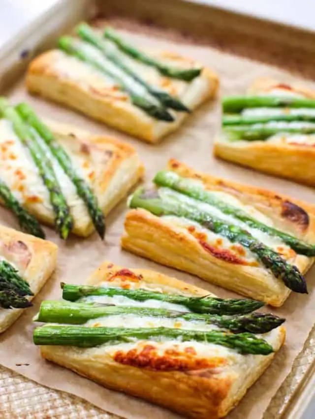Rectangular puff pastry tarts topped with cheese and asparagus spears make a delicious Easter party food, perfect for serving on a parchment-lined baking sheet.