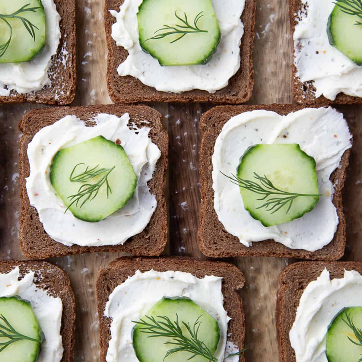 Squares of bread topped with cream cheese, a cucumber slice, and a sprig of dill arranged in a neat grid pattern—perfect as elegant Easter Party Food.