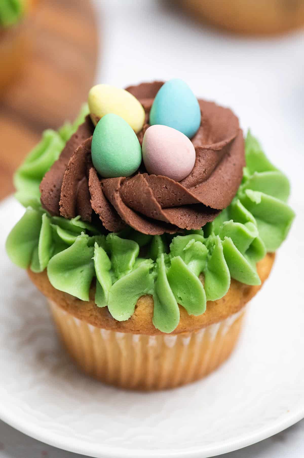 A cupcake decorated with green and brown frosting, topped with three candy eggs in yellow, blue, and pink—perfect as a festive Easter party food.