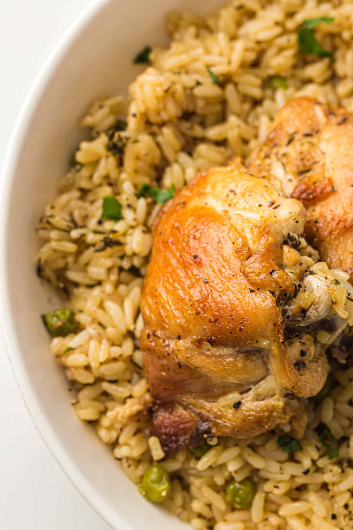 A bowl of seasoned Instant Pot Rice with peas, topped with a piece of golden-brown roasted chicken thigh.