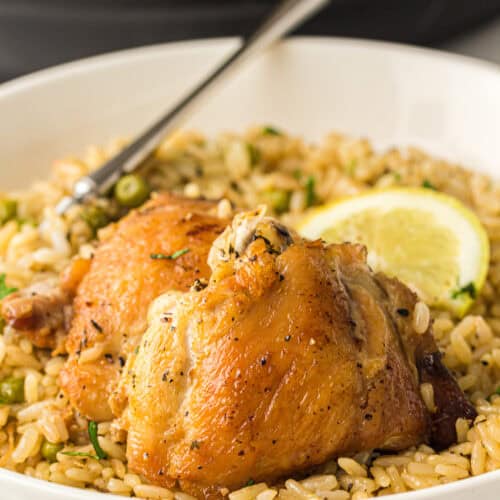 A bowl of seasoned rice topped with two roasted Instant Pot chicken thighs and a lemon slice, with a fork resting inside the bowl.