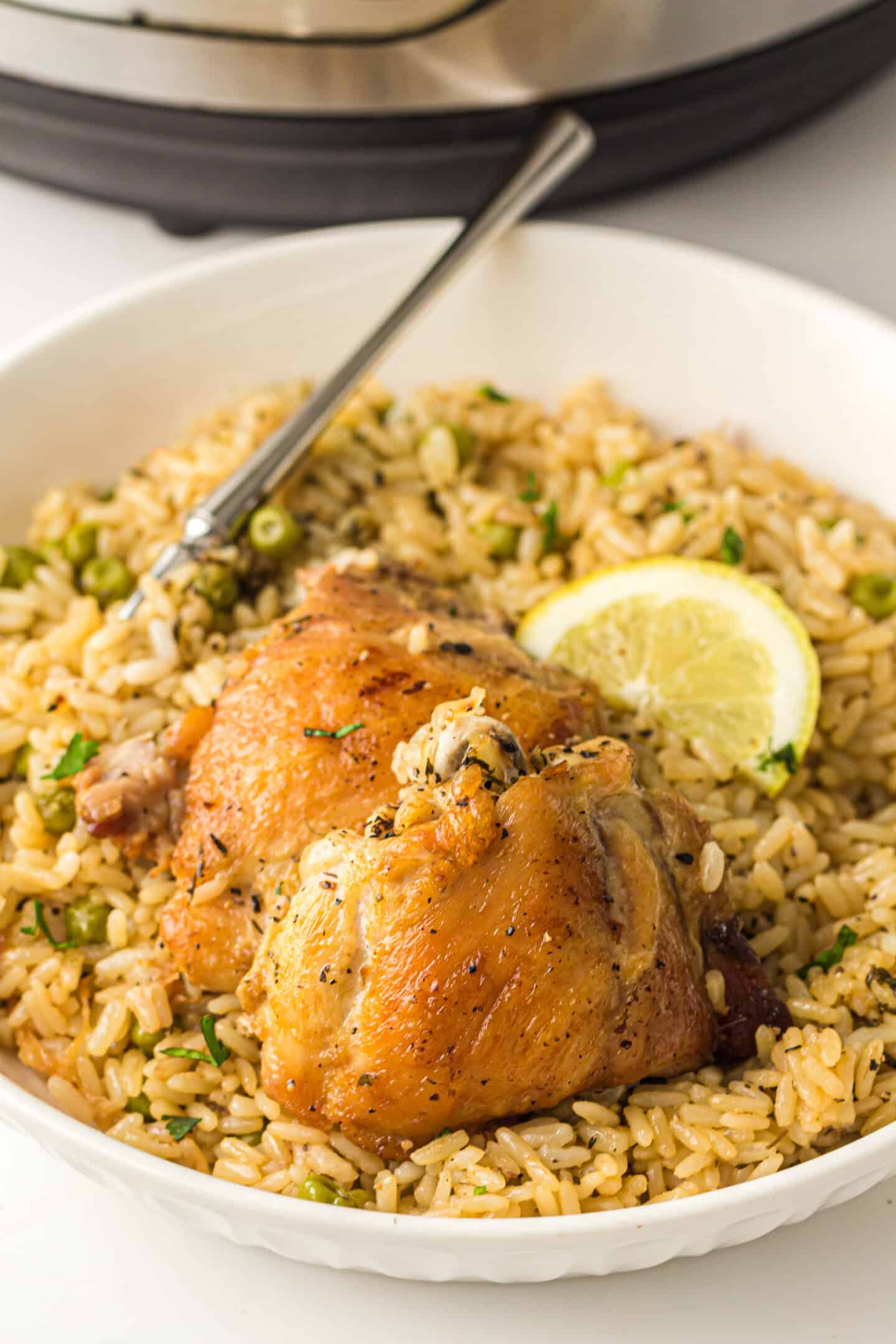 A plate of seasoned chicken thighs served on a bed of rice with herbs, peas, and a slice of lemon, with a fork resting on the side. Perfect for a quick and flavorful Instant Pot meal.
