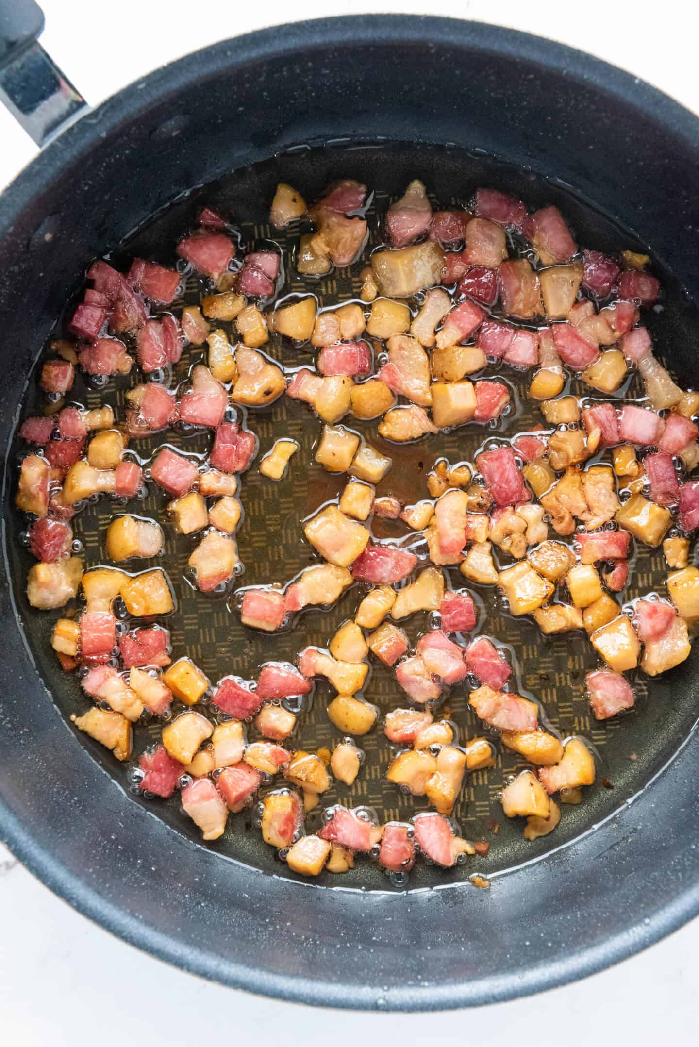 Diced bacon pieces sizzling and browning in a frying pan with rendered fat—perfect for preparing authentic Spaghetti Carbonara.