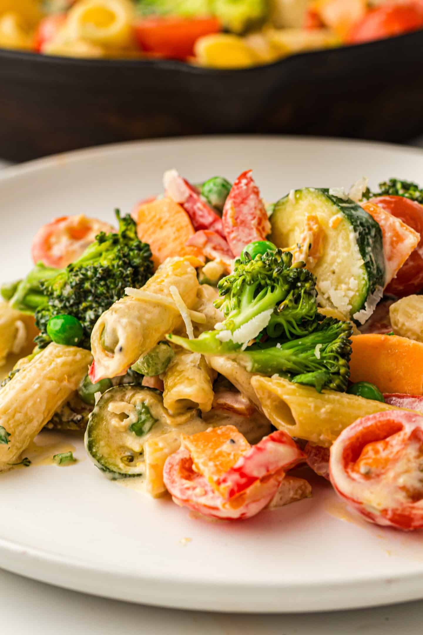 A plate of Pasta Primavera featuring penne pasta mixed with broccoli, zucchini, bell peppers, peas, and carrots in a creamy sauce, served on a white dish.