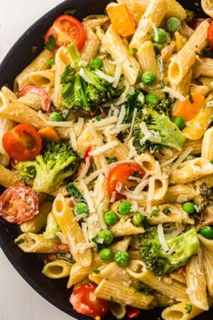 Enjoy this vibrant vegetarian pasta recipe featuring Pasta Primavera with broccoli, cherry tomatoes, peas, and shredded cheese in a skillet, garnished with fresh herbs.