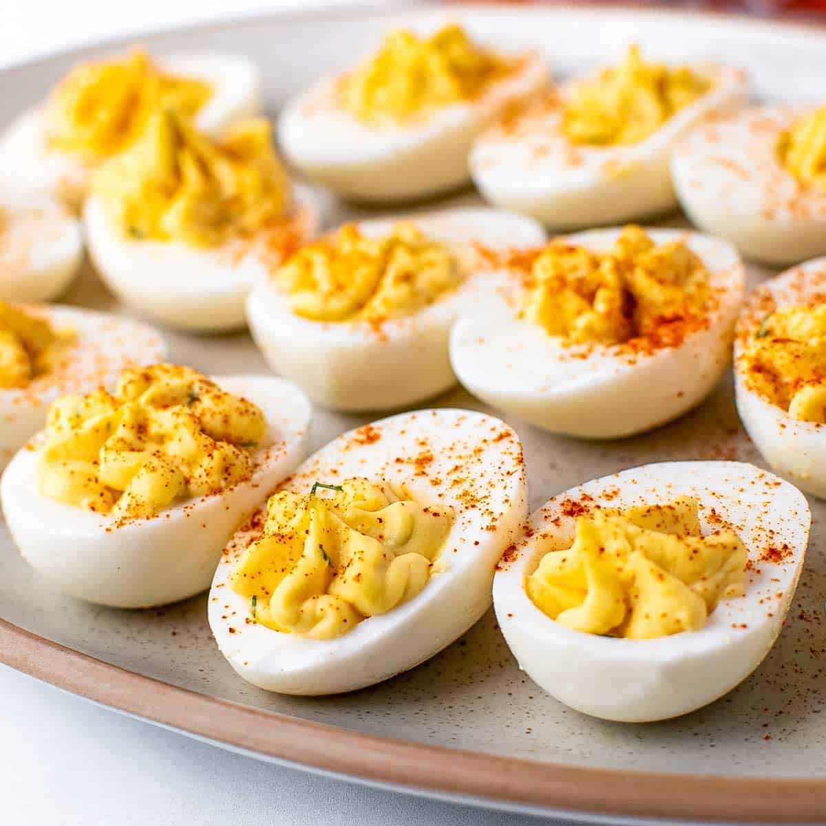 A plate of deviled eggs topped with paprika, arranged neatly on a beige dish—perfect as a classic Easter party food.