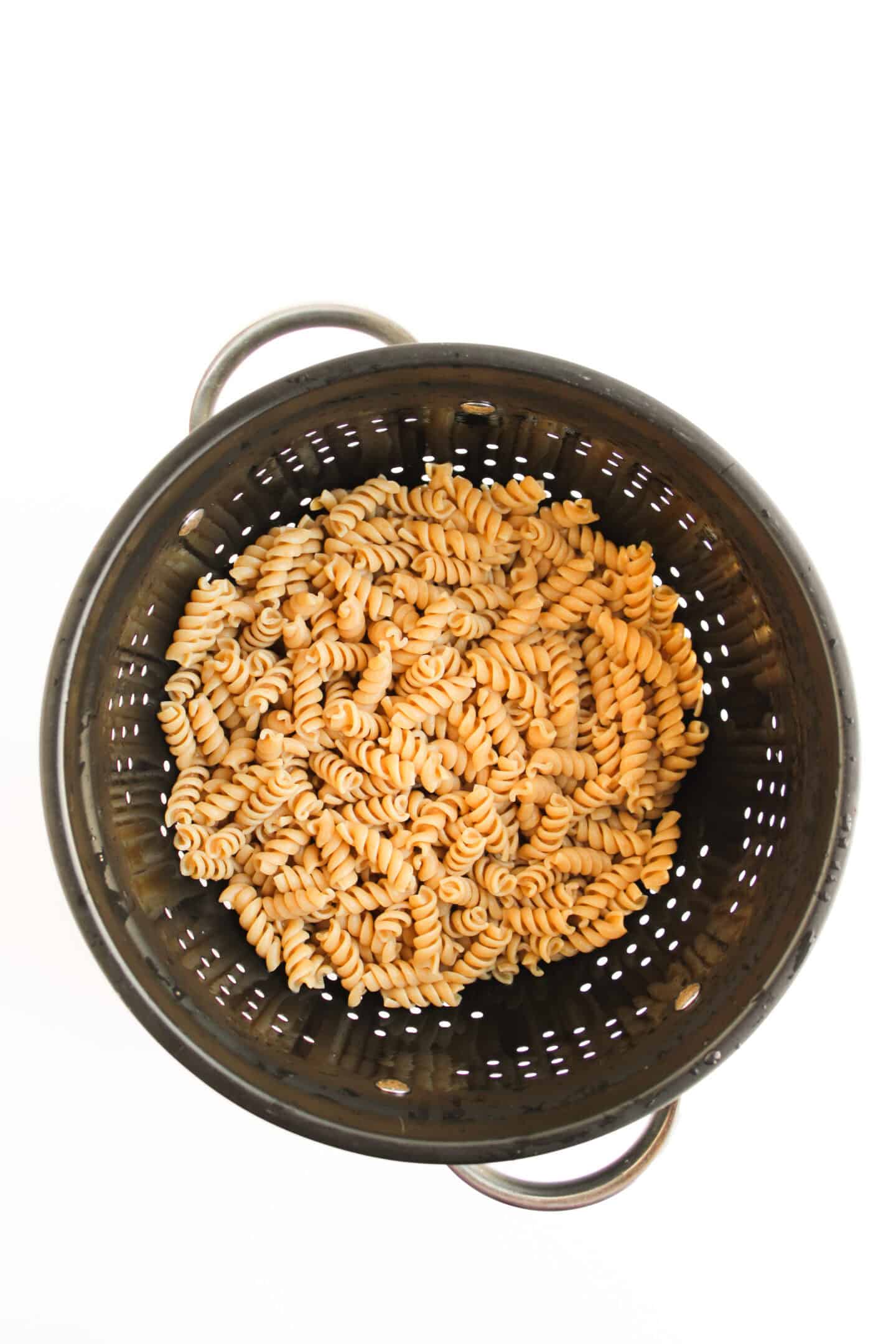 A metal colander filled with cooked rotini pasta, viewed from above on a white background—perfect for creating a healthy tuna pasta salad or mixing with creamy Greek yogurt.