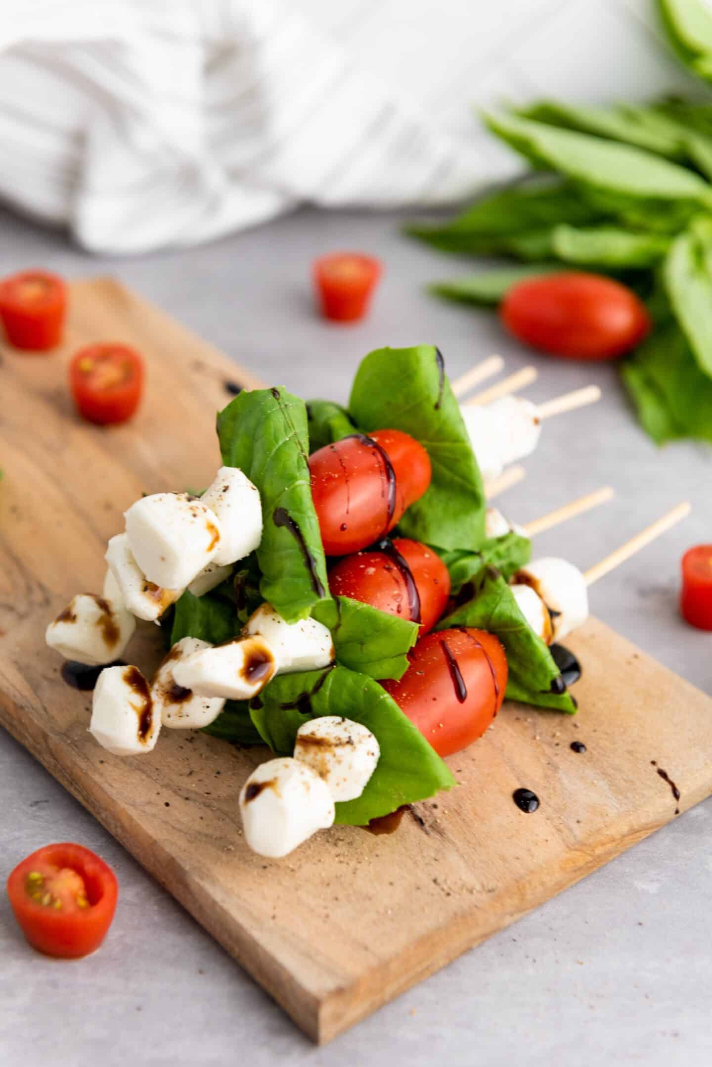 Spring Appetizers shine with skewers of mozzarella balls, cherry tomatoes, and basil leaves, drizzled with balsamic glaze and artfully arranged on a wooden board with scattered tomatoes and basil in the background.
