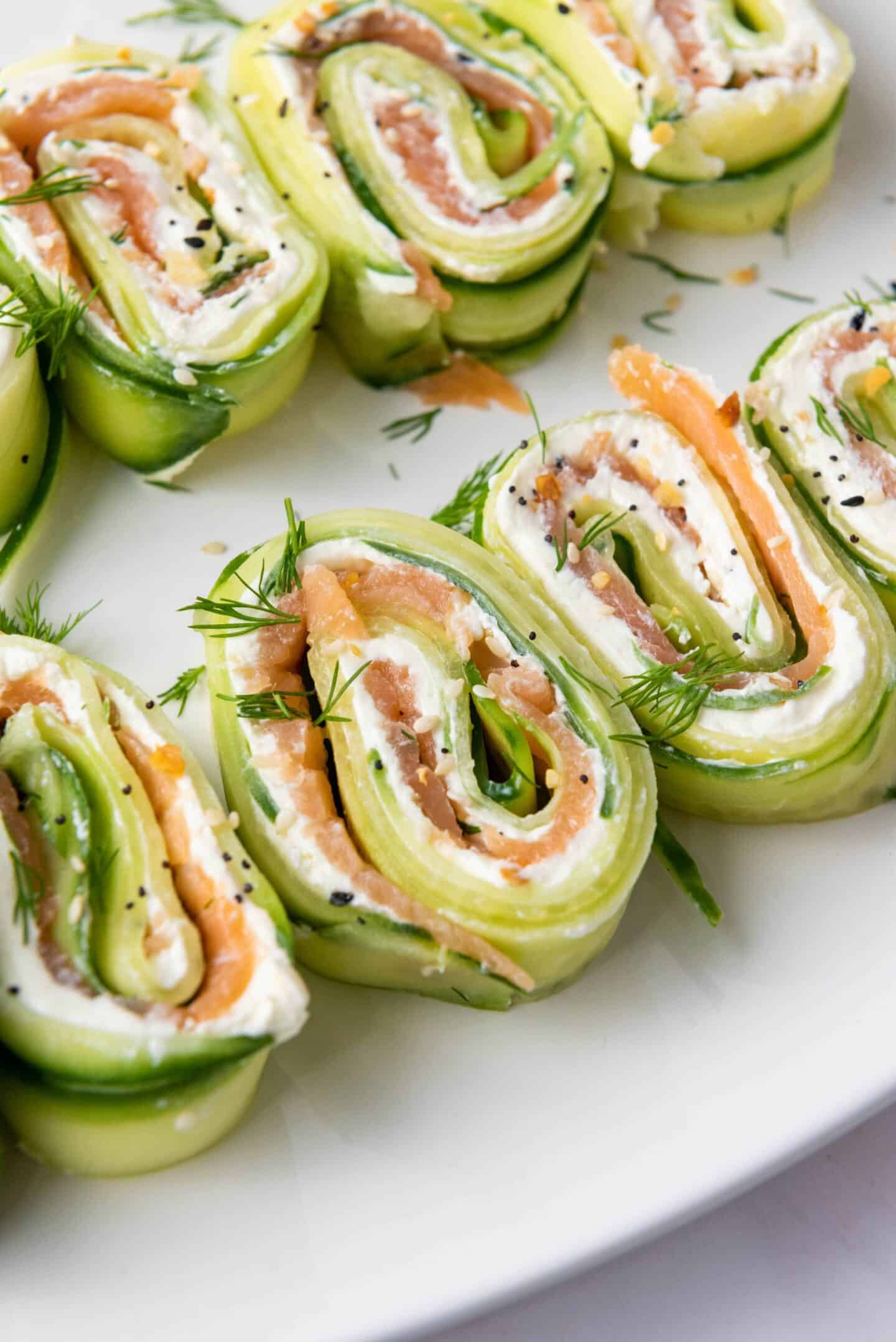 Sliced cucumber roll-ups filled with cream cheese, smoked salmon, and herbs make refreshing Spring Appetizers, beautifully arranged on a white plate.