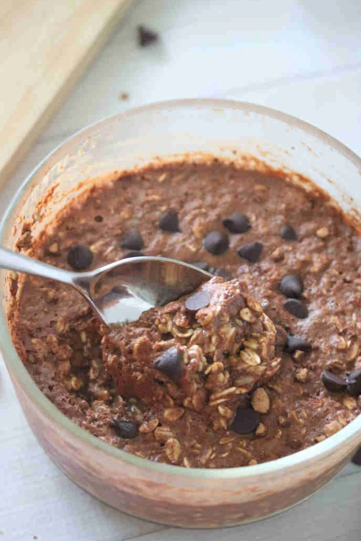 A glass bowl filled with baked chocolate oatmeal—made without chia seeds—topped with chocolate chips; a spoon is scooping out a portion.